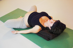 Schwangere macht Yoga.Hier in Rückenlage, unterstützt, Beine angewinkelt.