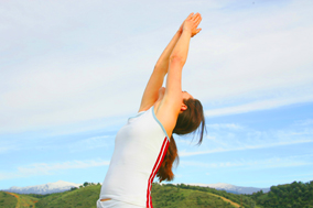 Yogalehrerin macht Yoga Rückbeuge vor blauem Himmel und grünen Bergen